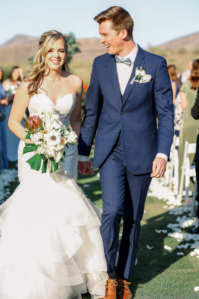 Groom and bride holding bouquet walking down aisle,