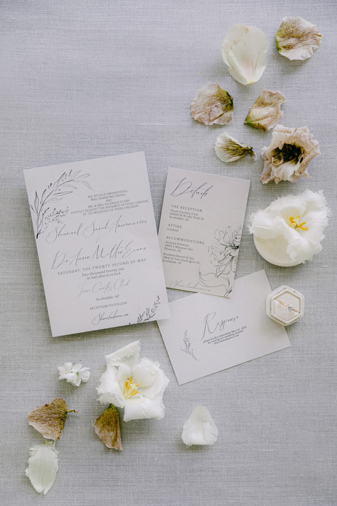 Wedding invitation and ring flat lay with flowers and petals around it.