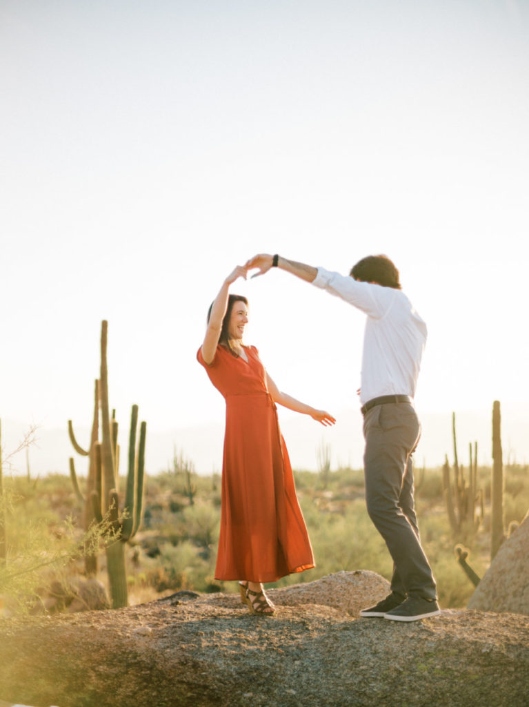 Woman and man dancing on large boulder in desert.