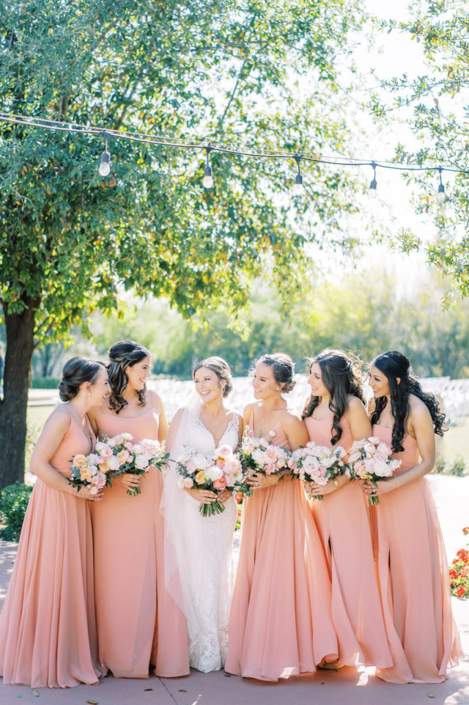 Bride and bridesmaids standing together smiling, holding bouquets.