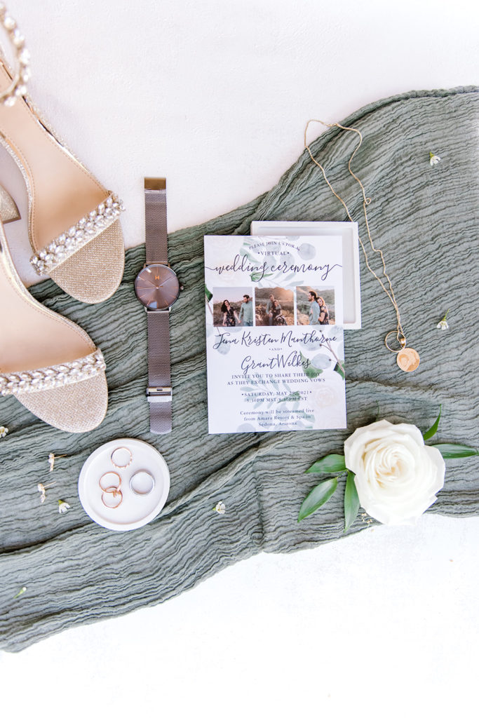 Wedding details of invitation, bride shoes, necklace, groom watch, rings, and flowers.