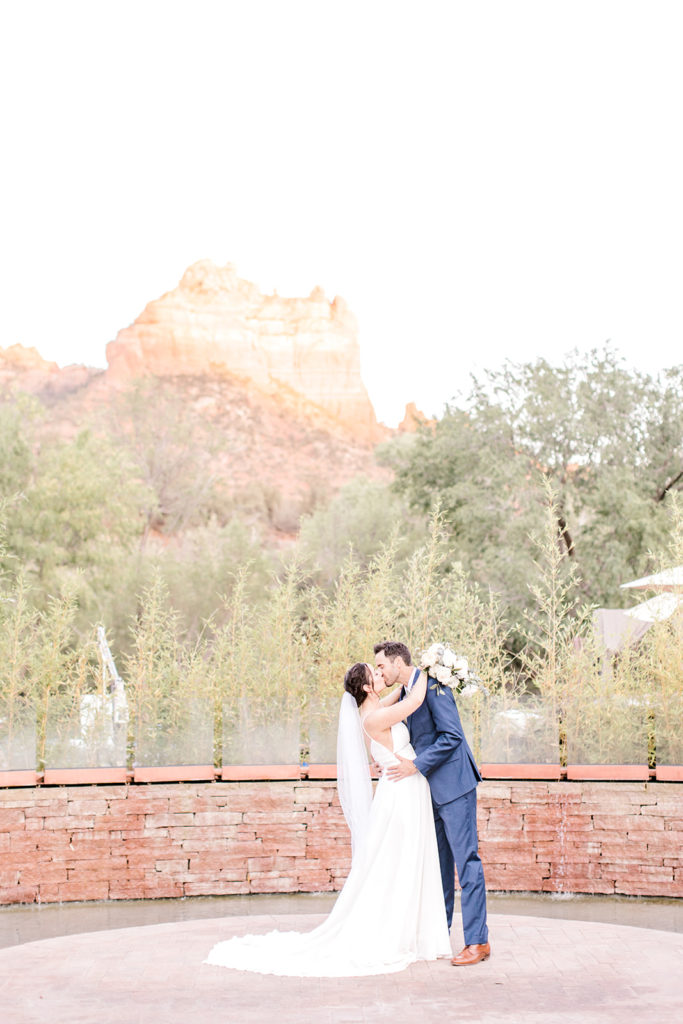 Bride and groom kissing, embracing in front of Sedona landscape.
