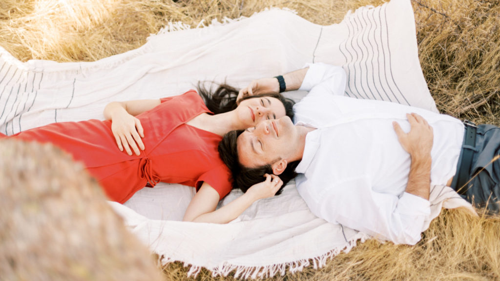 Man and woman lying down on white blanket next to each other.
