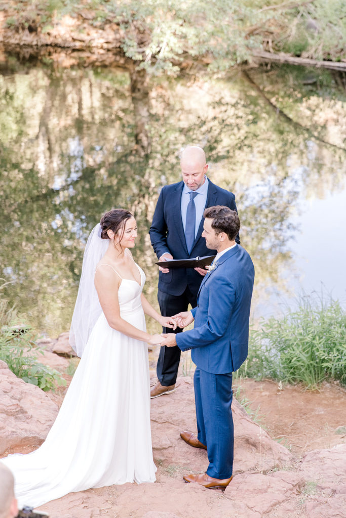 Bride, groom, and officiant during outdoor wedding ceremony by lake in Sedona.