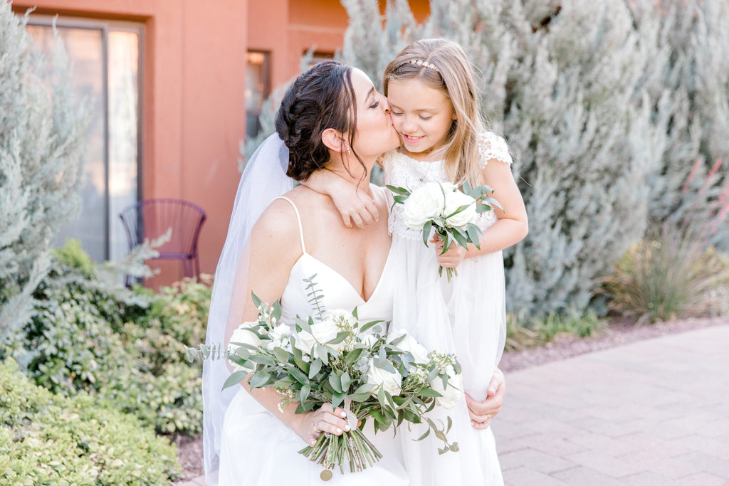 Bride kissing flower girl on cheek, both holding bouquets.