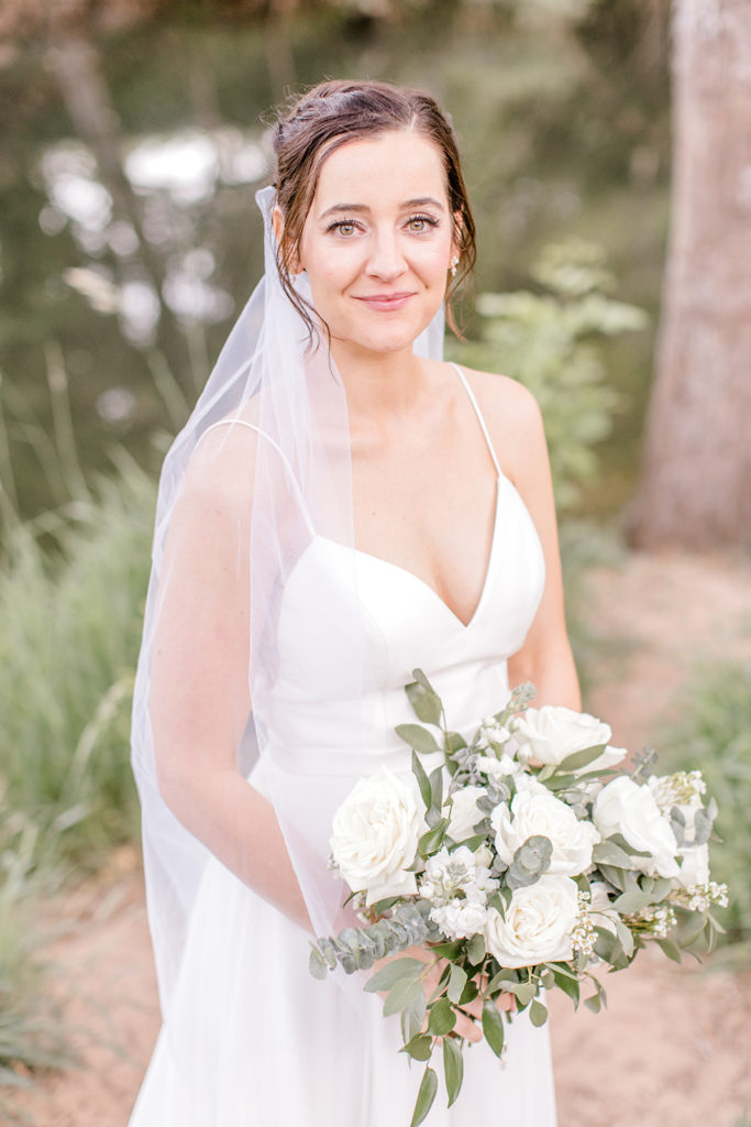 Bride in wedding dress holding bouquet of white flowers and greenery.