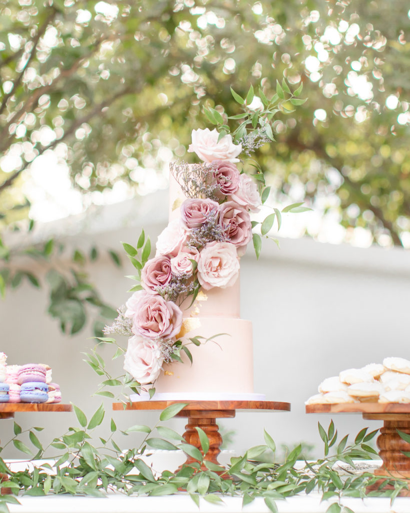 Three tiered wedding cake in light pink with gold flakes and pink and mauve roses.