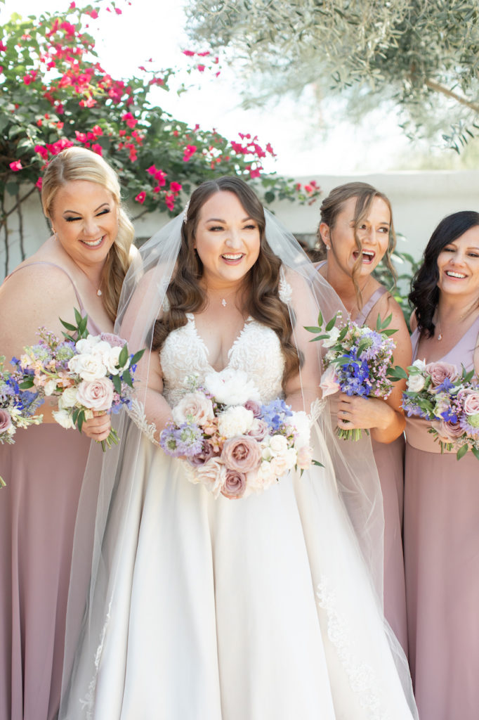 Bride and bridesmaids holding bouquet, laughing.