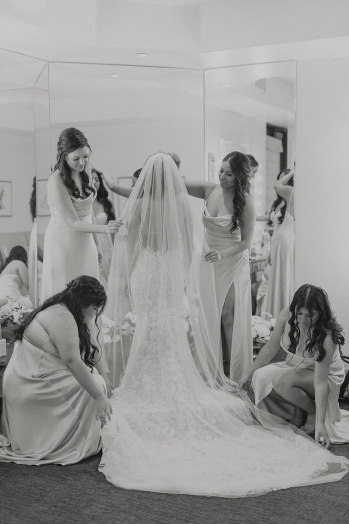 Bridesmaids helping bride get ready in veil and dress.
