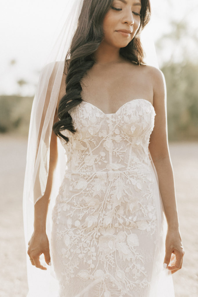 Bride looking down in embroidered white dress with long veil.