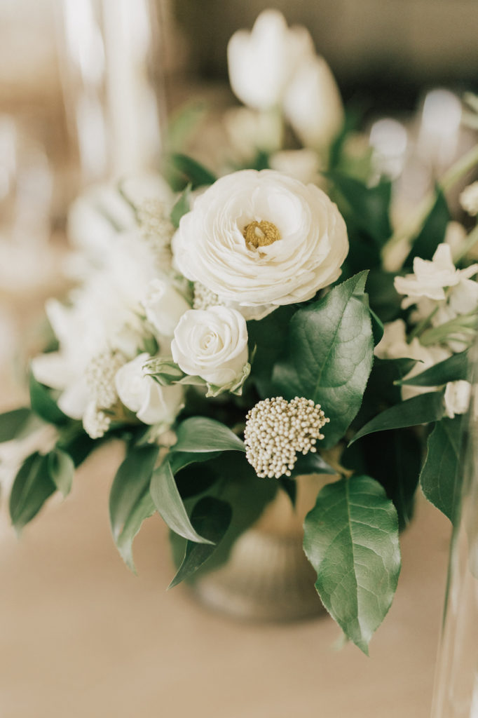Close of of white flowers and greenery wedding reception centerpiece in gold vase.