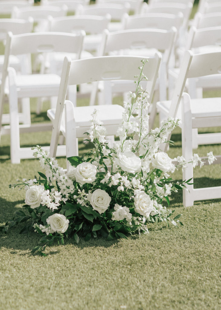 Back of wedding ceremony aisle white floral ground arrangement.