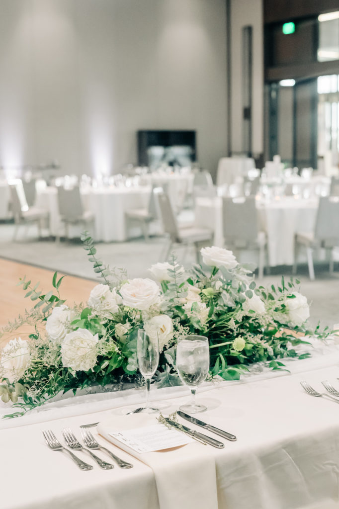 Head table floral arrangement of white flowers and greenery.
