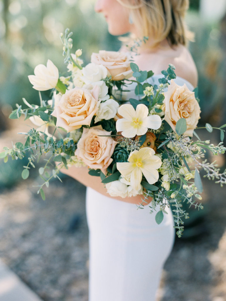 Lush bridal bouquet of peach roses, yellow flowers, and greenery.