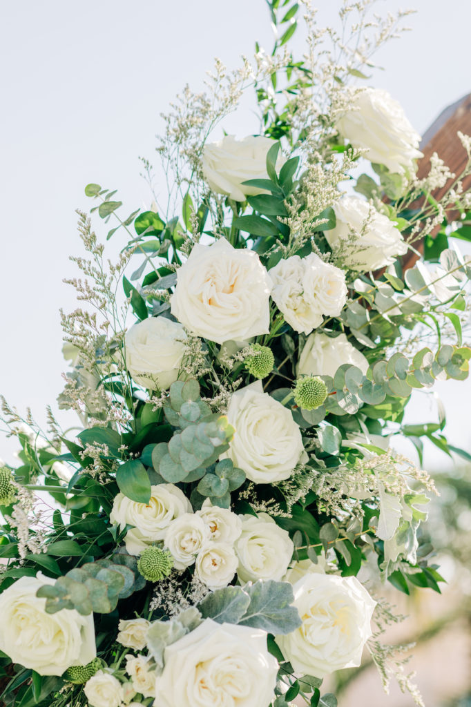 White flowers, including roses, and greenery in ceremony wedding flowers installation.