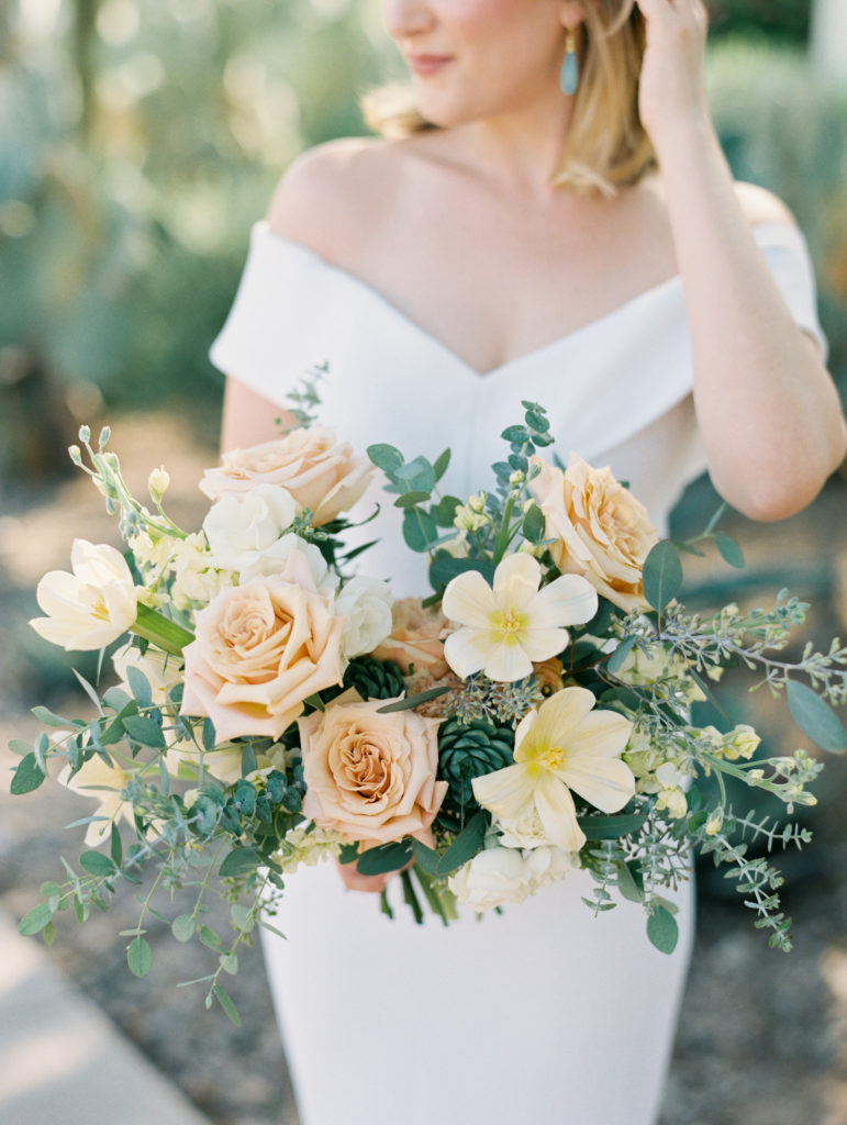 Bride holding lush bridal bouquet of peach and yellow flowers.