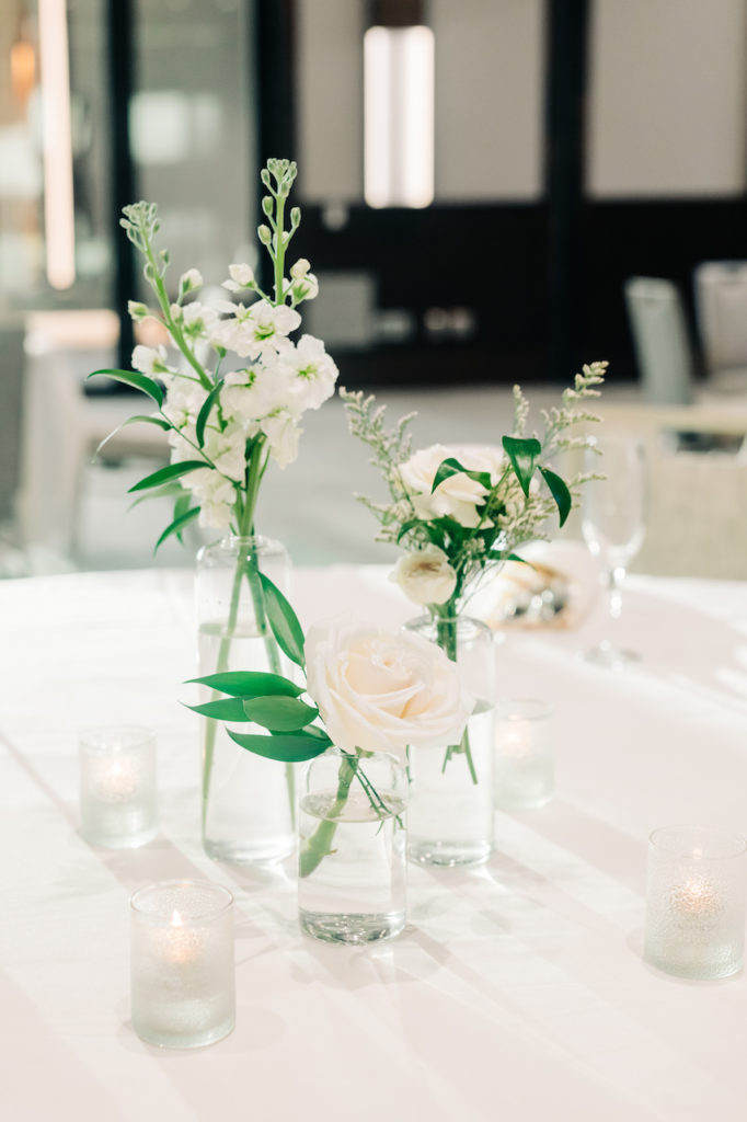 Three white flowers and greenery bud vases at wedding reception.