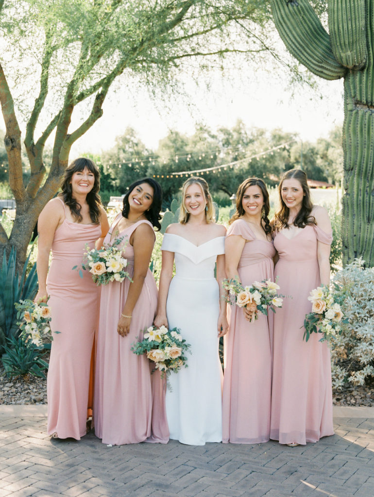 Bride with bridesmaids in blush dresses holding bouquets.