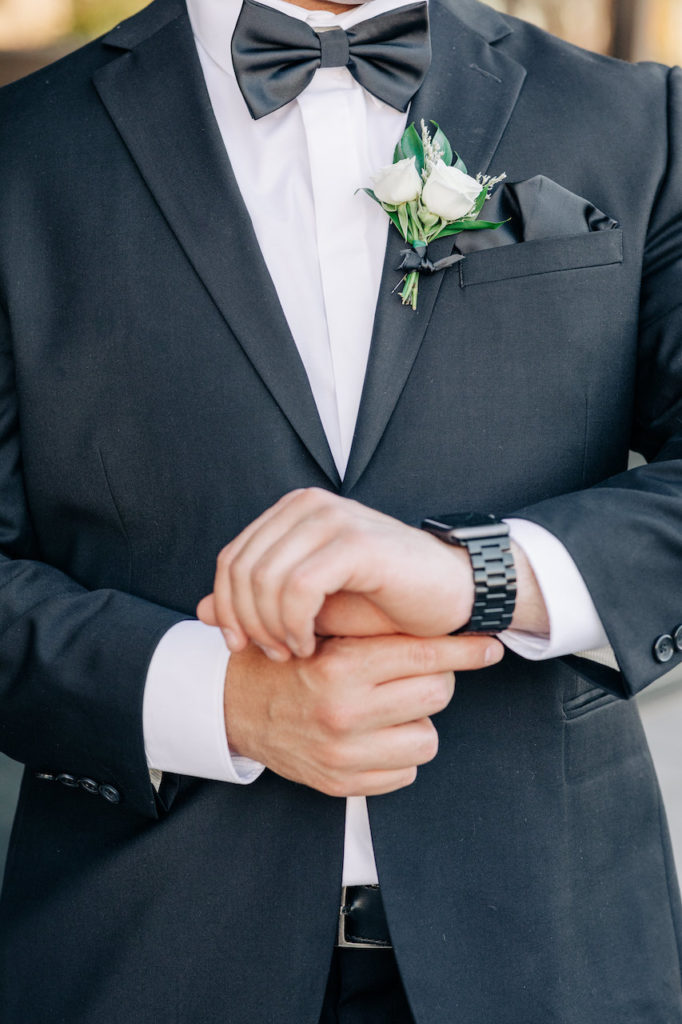 Groom in black suit with boutonniere of white roses and greenery.