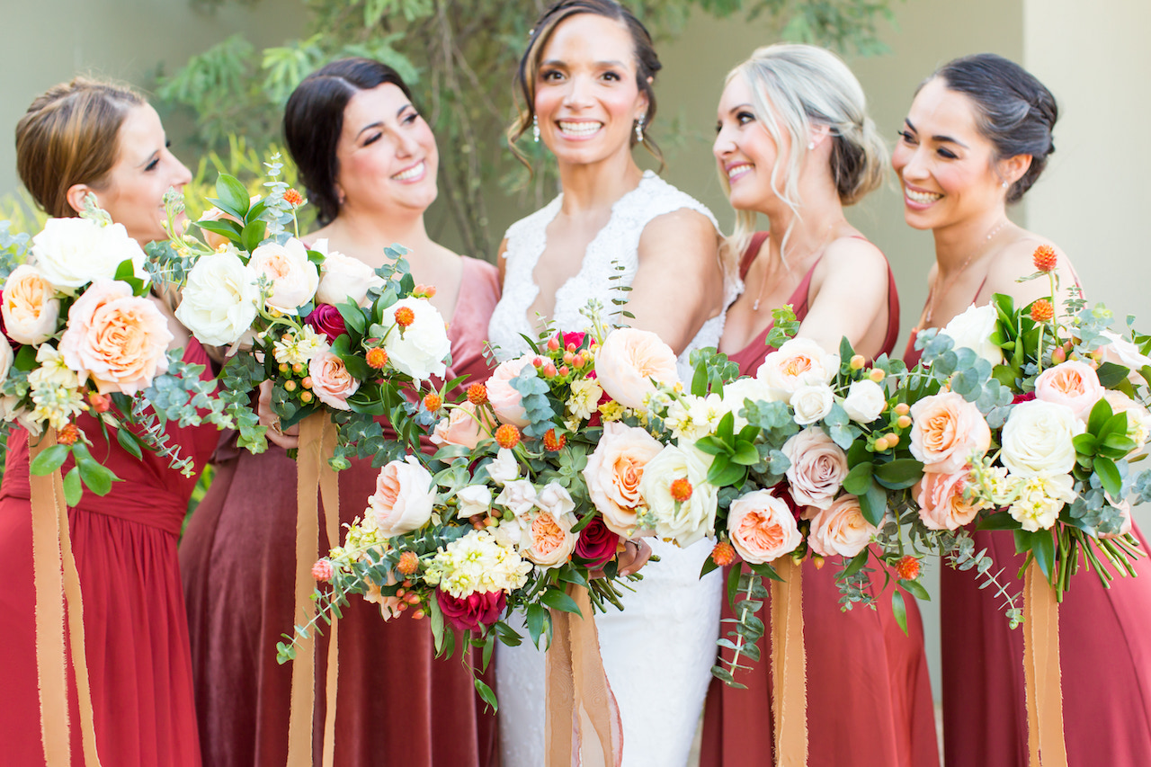 Bridesmaids in rust red dresses with bride all holding bouquets.