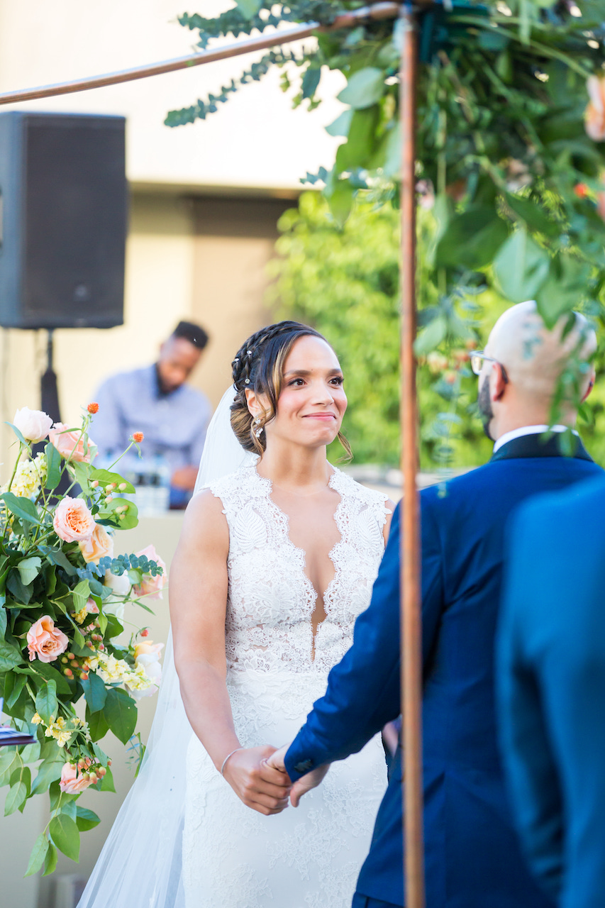 Wedding ceremony under arch, bride smiling.