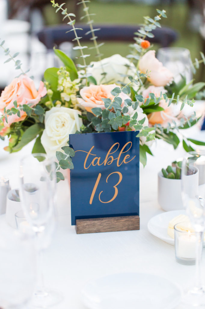 Reception table number of blue acrylic and rose gold writing in front of centerpiece.