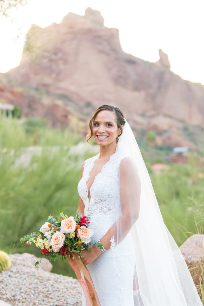 Bride holding bouquet of roses and greenery, smiling.