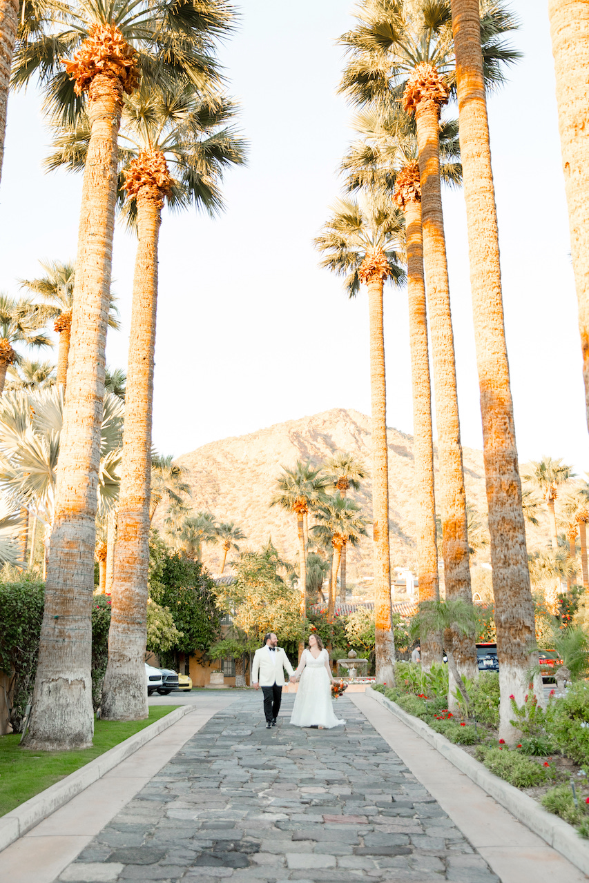 Bride and Groom holding hands walking down stone street lined with palm trees at Royal Palms.