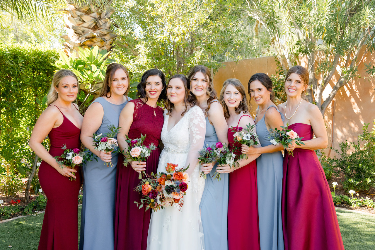 Bridesmaids with bride, all holding bouquets, posing outside.