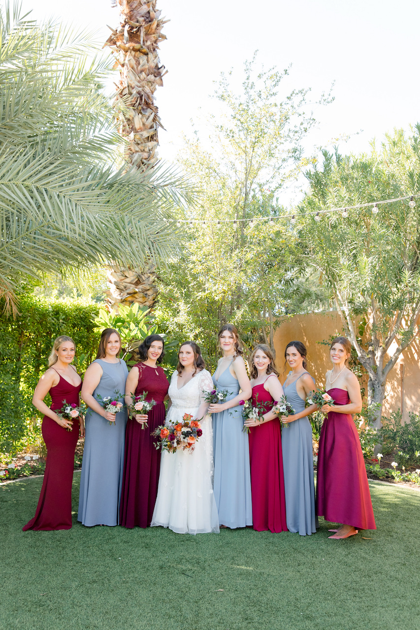 Bridesmaids in light blue and maroon dresses with bride outside in line, all holding bouquets.