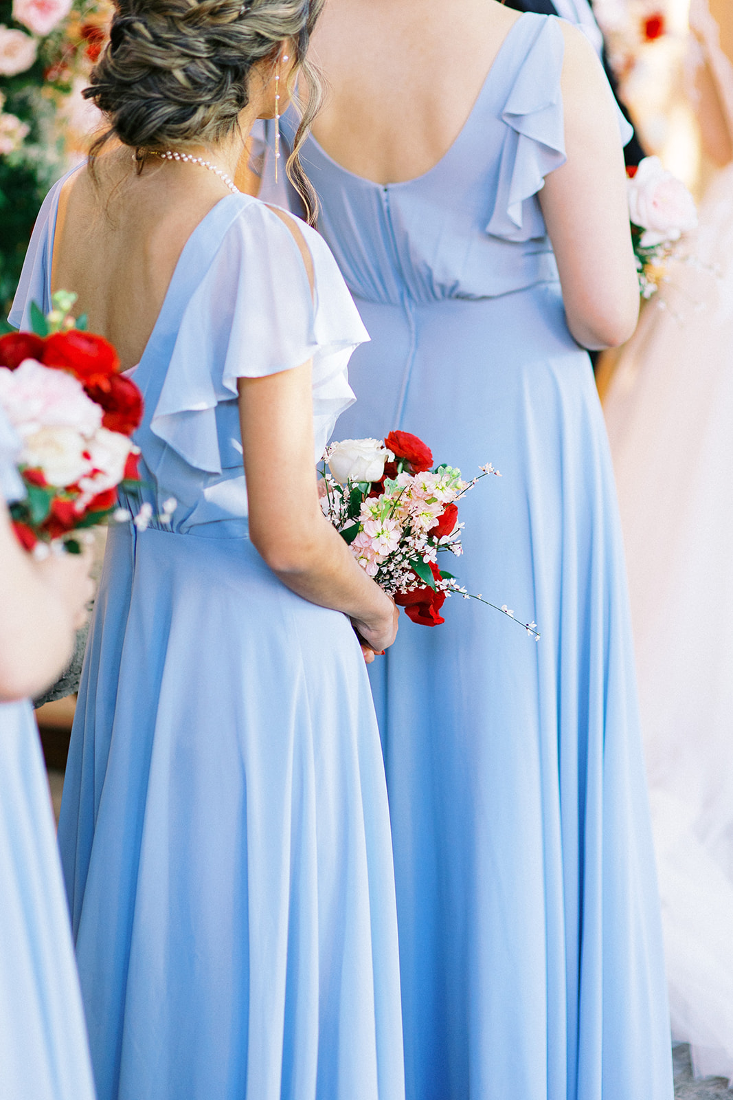 Backs of bridesmaids wearing light blue dresses facing towards bride at wedding ceremony, holding bouquets.