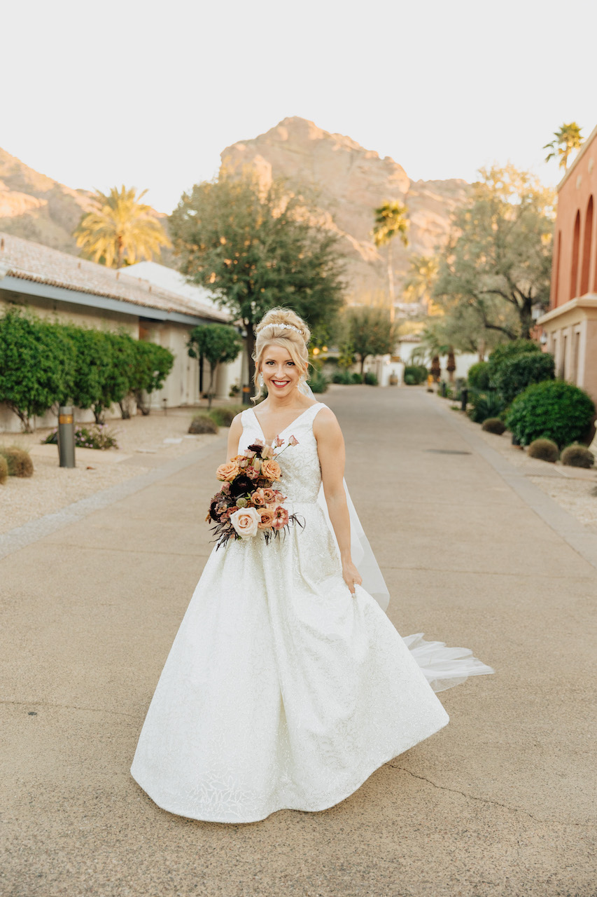 Bride smiling and walking while holding bouquet at Arizona wedding.