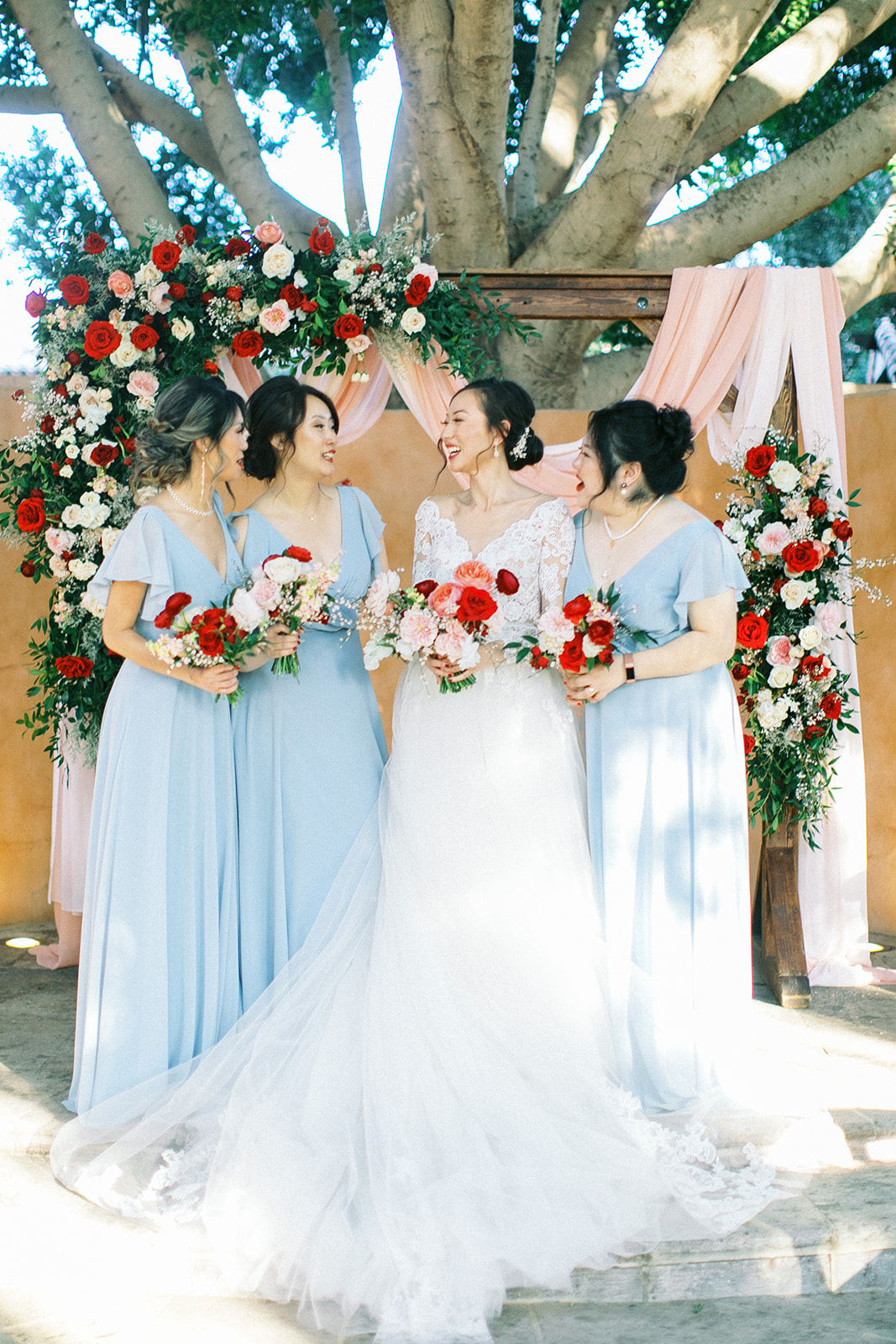 Bridesmaids in light blue dresses with bride in front of ceremony altar, all holding bouquets.