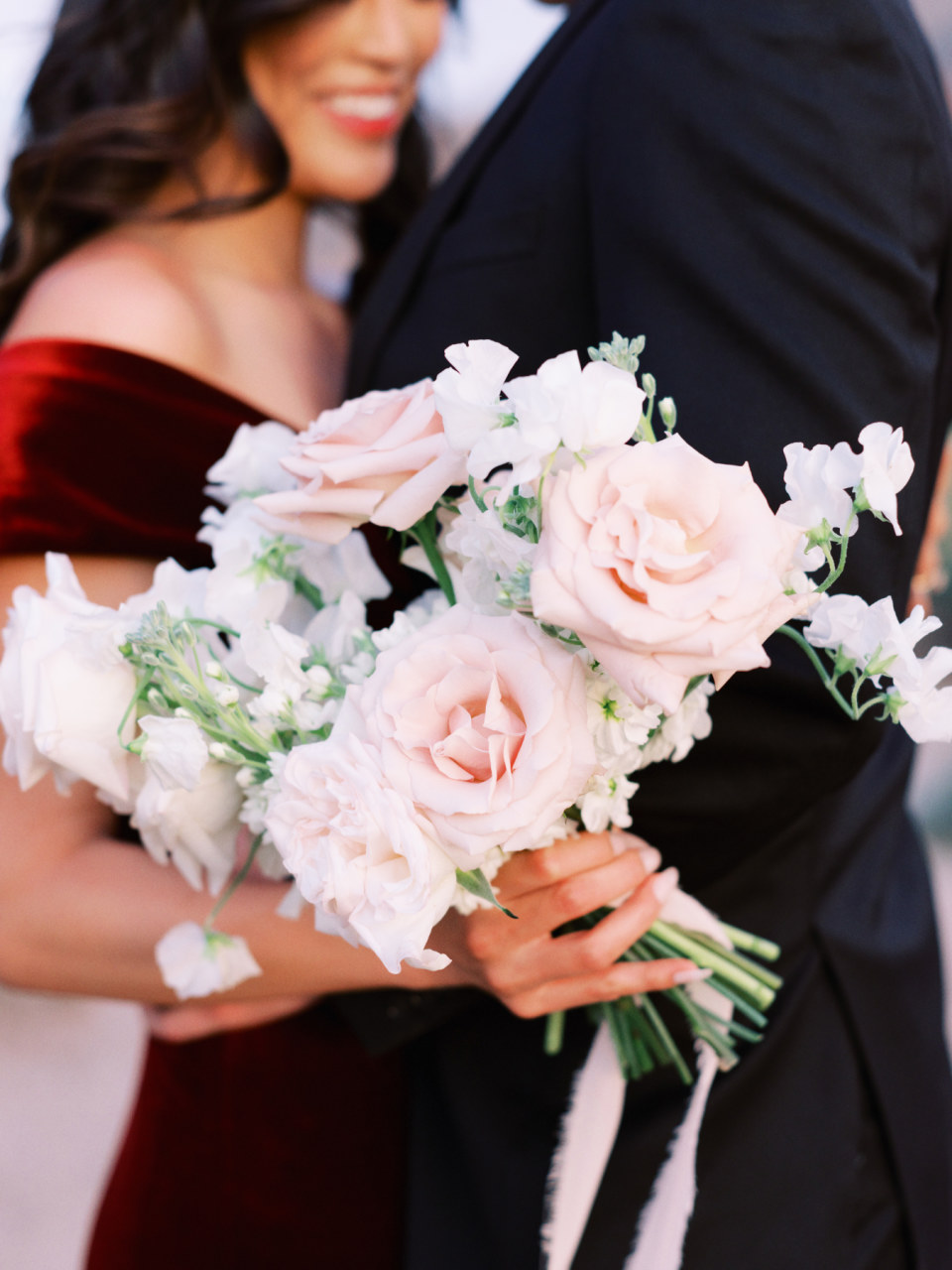 Woman and man in background with bouquet of pink pale flowers and white flowers in her hand.