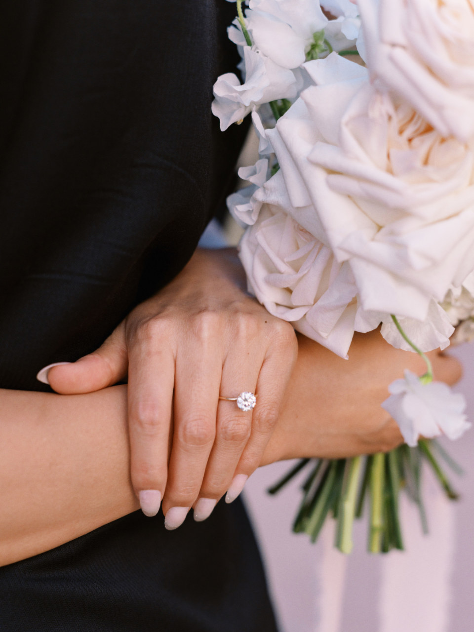 Engagement ring on woman's hand holding bouquet of pale pink flowers.