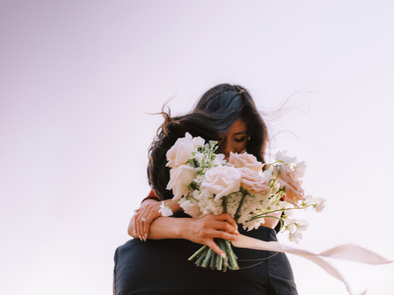 Man lifting up woman, embracing. Woman holding light pink and white flowers bouquet.