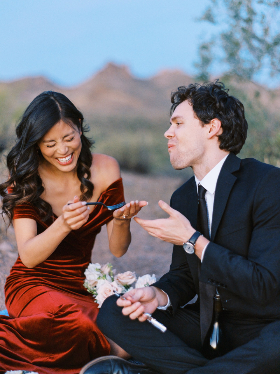 Woman laughing holding fork up and man chewing and laughing.