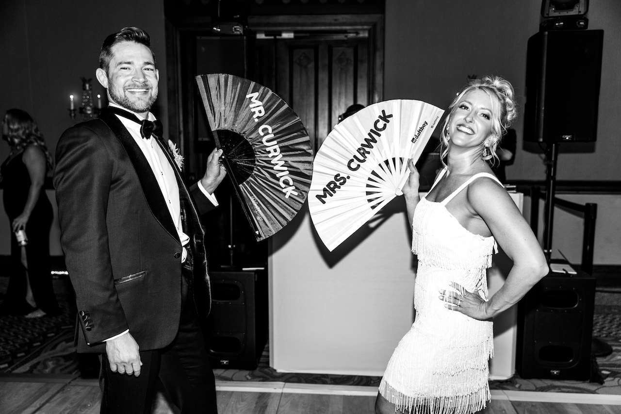Bride and groom smiling, holding custom fans with their names.