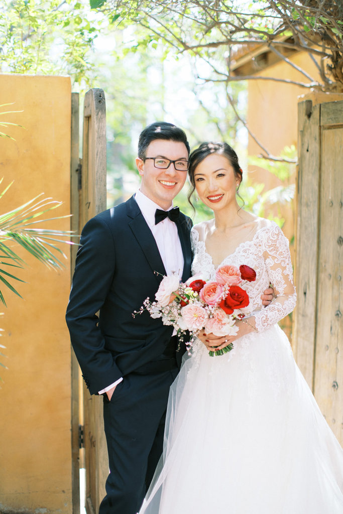 Bride and groom smiling, standing next to each other in front of open wood doors.