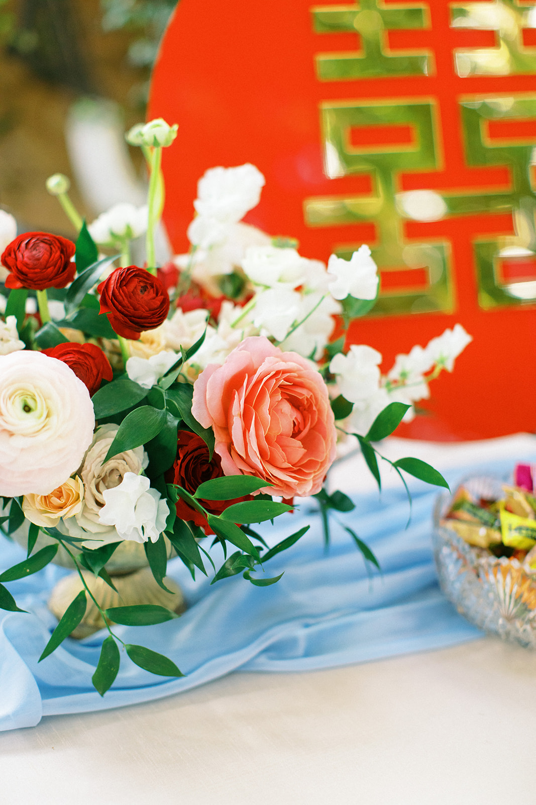 Reception centerpiece of white, pink, and red flowers with greenery in gold vase.