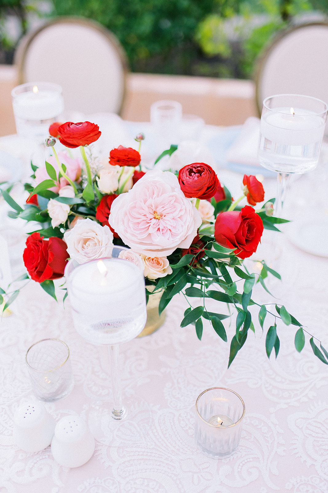 Short wedding reception centerpiece in gold vase of red, pink, and white roses and greenery.