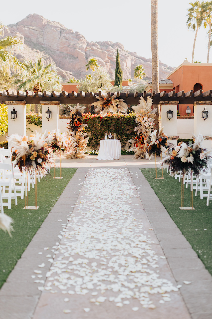 White rose petals down outdoor wedding ceremony aisle.