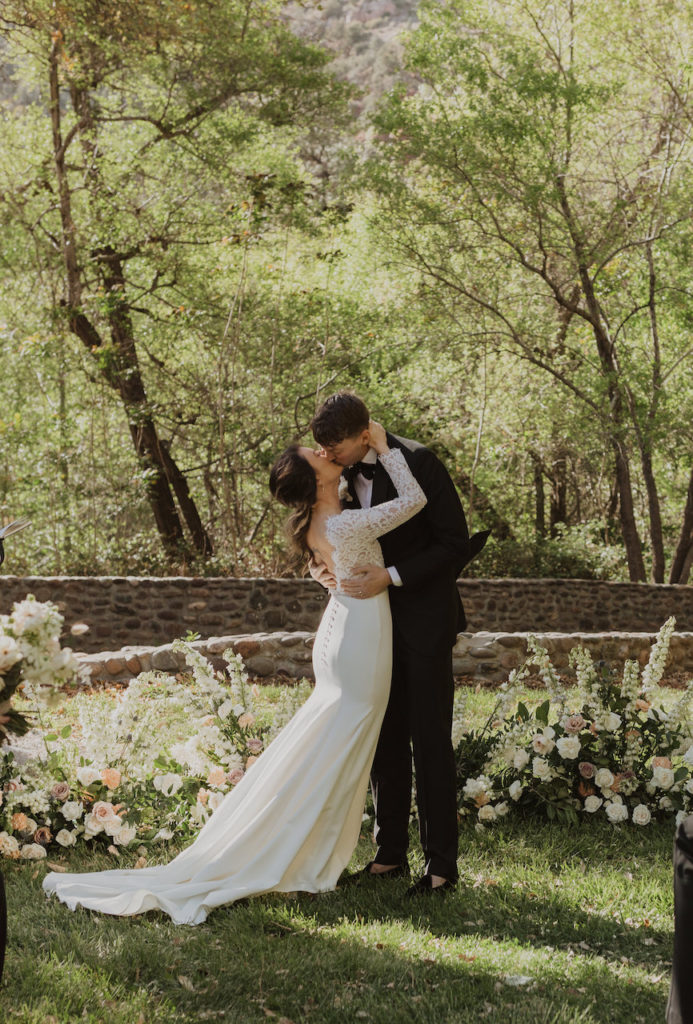 Sedona, Arizona outdoor wedding reception with bride and groom kissing in front of trees, ground floral arrangements.
