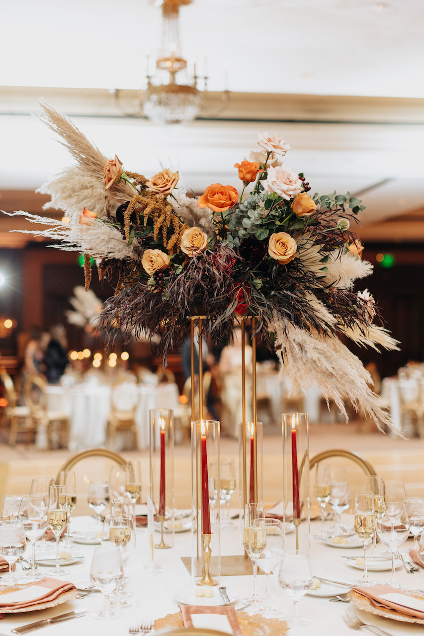 Tall wedding reception centerpiece on brass holder with roses and dried elements of pampas.