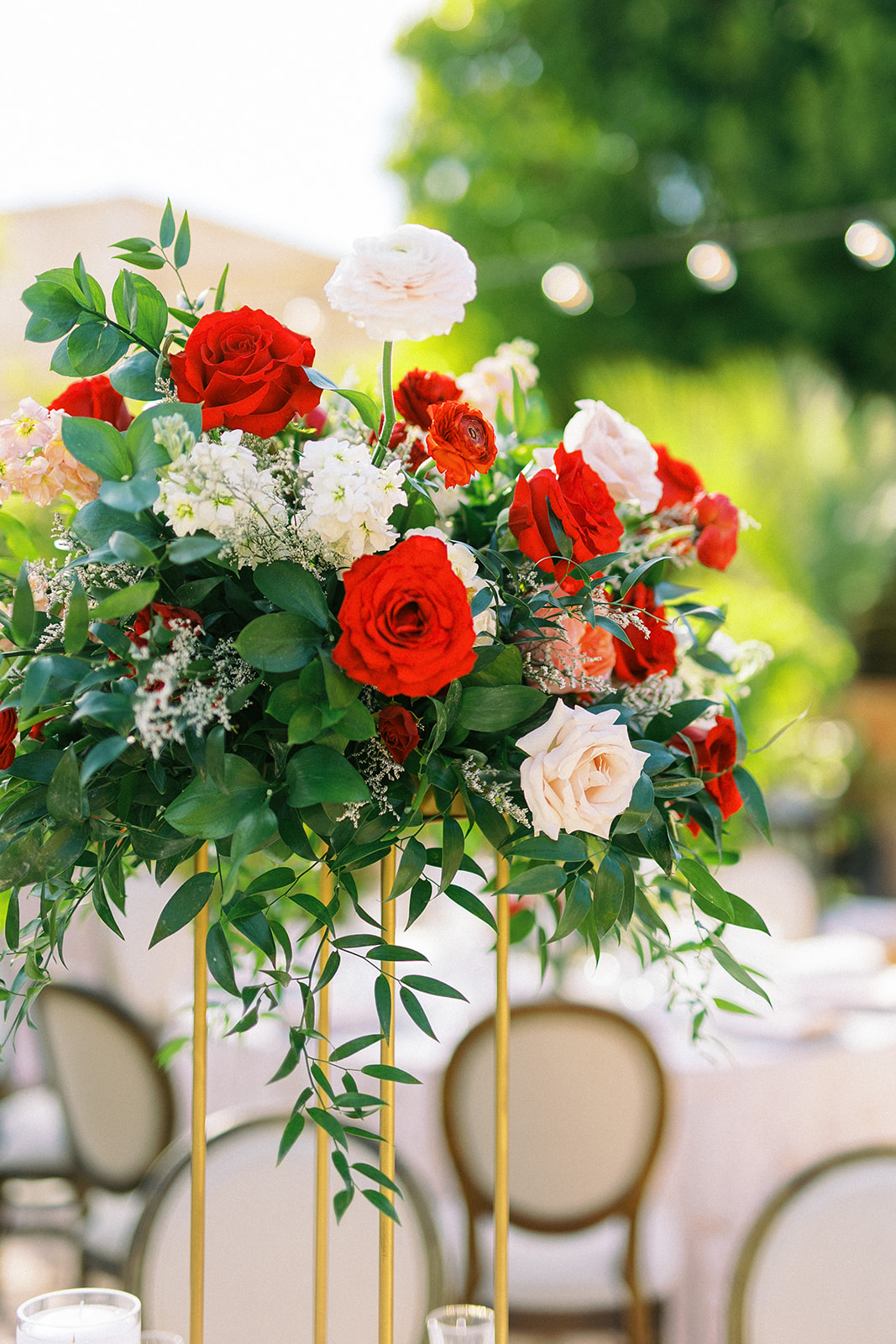 Tall gold wedding reception centerpiece of greenery and pink, red, and white flowers.