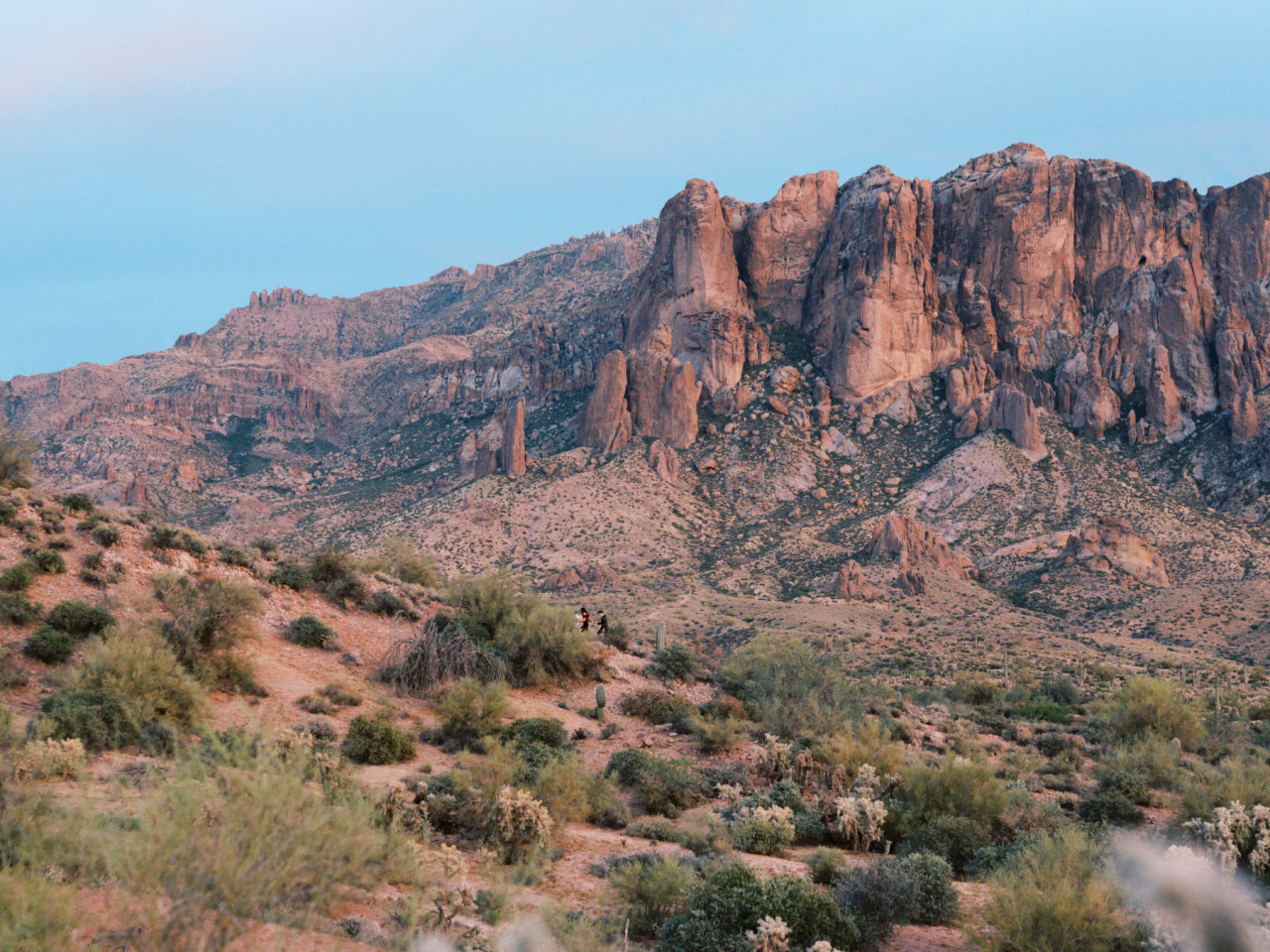 Superstition Mountain desert landscape with woman in man in far distance walking up slope.