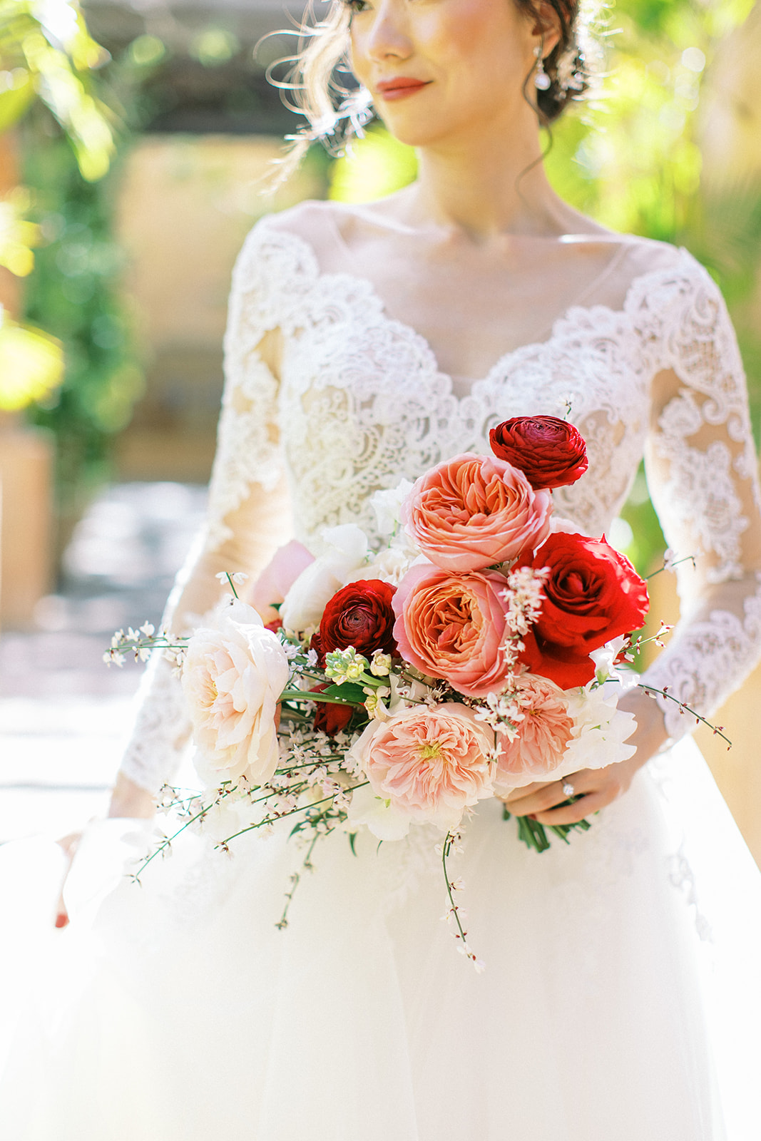Bride looking off, holding bouquet of large pink, white, and red roses.