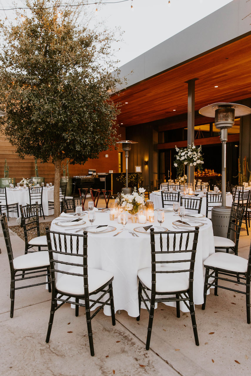 Outdoor wedding reception with low and high white flower centerpieces.