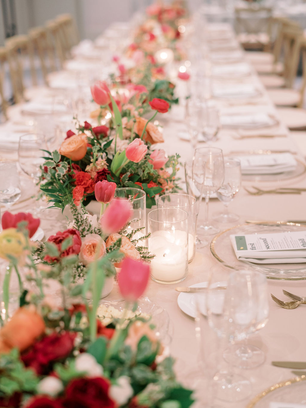 Long table at wedding reception with varied floral centerpieces down center.