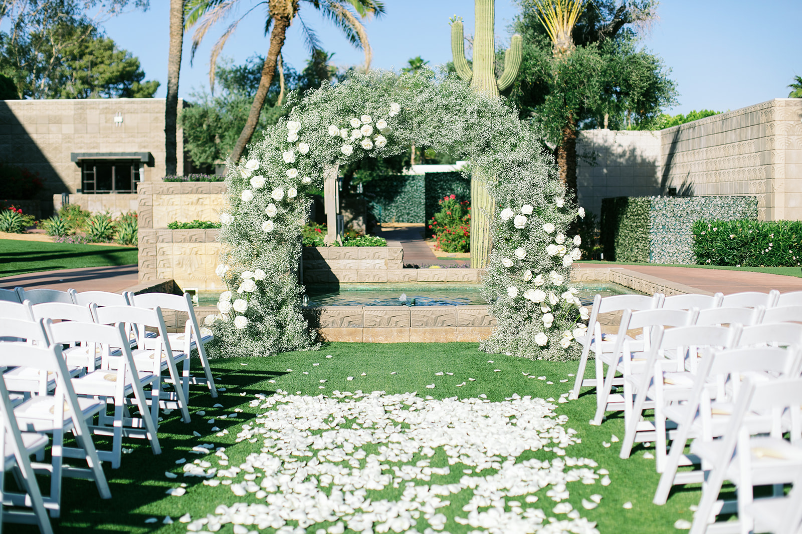Baby's breath wedding ceremony arch with white roses and white rose petals down aisle.